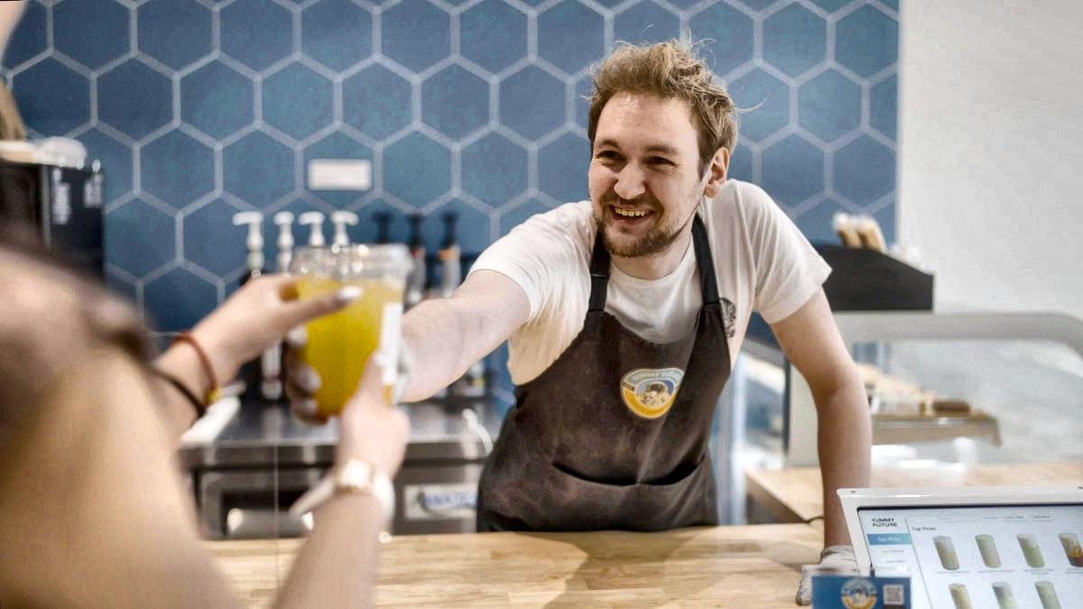 A store lead handing a fresh juice across the counter to a customer